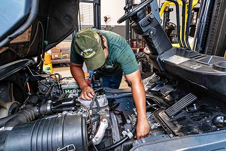 Reparos em empilhadeiras Técnico realizando reparo no compartimento do motor de uma empilhadeira