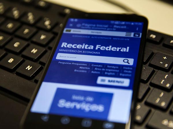 Imposto de Renda e declaração de impostos Celular com o portal da Receita Federal aberto sobre teclado, para declaração de Imposto de Renda