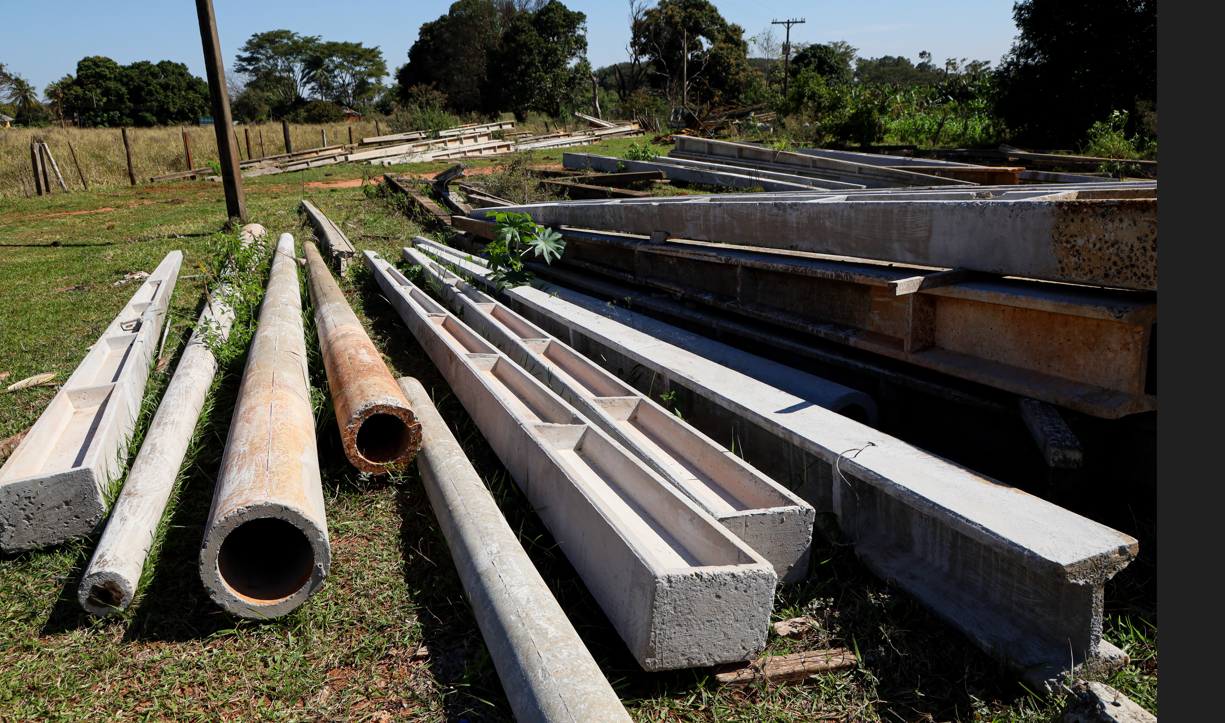 Postes de concreto de seção circular em primeiro plano, ao lado de postes Duplo T no pátio da Lahos
