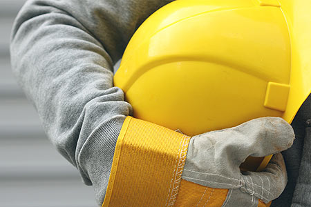 Direito Trabalhista Trabalhador com luvas de proteção segurando capacete amarelo