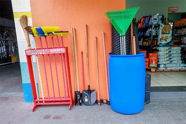 Produtos de higiene, limpeza e utilidades Vassouras, rastelos, enxadas, pás e caixa d'água expostos na frente da loja