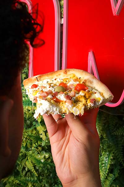 Fatia de pizza salgada Mão segurando uma fatia de pizza salgada em frente a letreiro neon vermelho