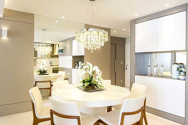 Sala de jantar com parede espelhada, lustre de cristal e armário com portas de vidro