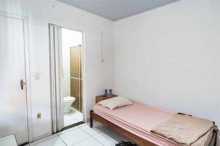Quarto individual com banheiro Quarto individual com cama de solteiro, criado-mudo e porta aberta para o banheiro da suíte