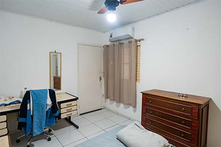 Quarto com ar-condicionado Quarto com ar-condicionado, cômoda de madeira, escrivaninha e ventilador de teto