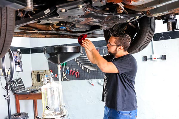 Troca de óleo e de filtros Mecânico da MS Lubrificantes drenando o óleo do motor com o veículo no elevador