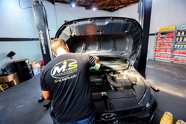 Troca de óleo do carro na MS Lubrificantes Profissional da MS Lubrificantes verificando o motor de um carro com o capô aberto na oficina