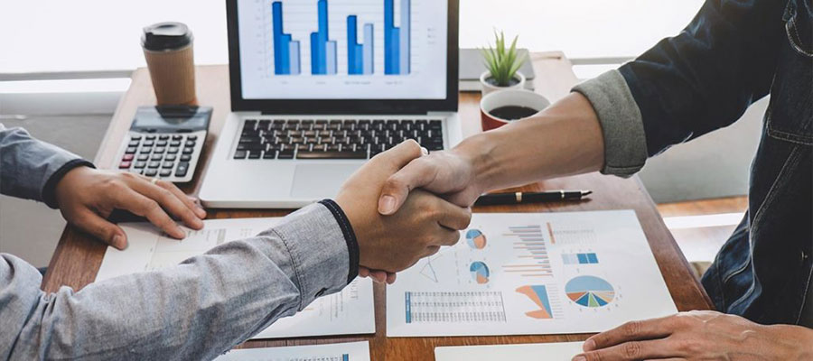 Aperto de mãos sobre mesa com relatórios e gráficos fiscais Aperto de mãos sobre mesa com relatórios e gráficos fiscais
