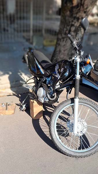 Troca de pneu de moto no local – Borracharia Móvel do Fabrício Motocicleta preta apoiada em calço de madeira na calçada durante troca do pneu traseiro no local