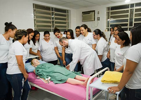 Professor demonstrando procedimento em manequim durante aula prática de enfermagem